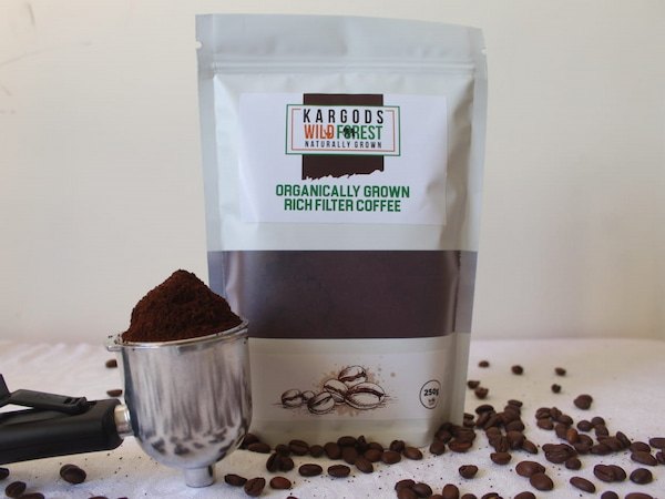 Kargods Wild Forest rich filter coffee pouch beside a portafilter of ground coffee and roasted beans
